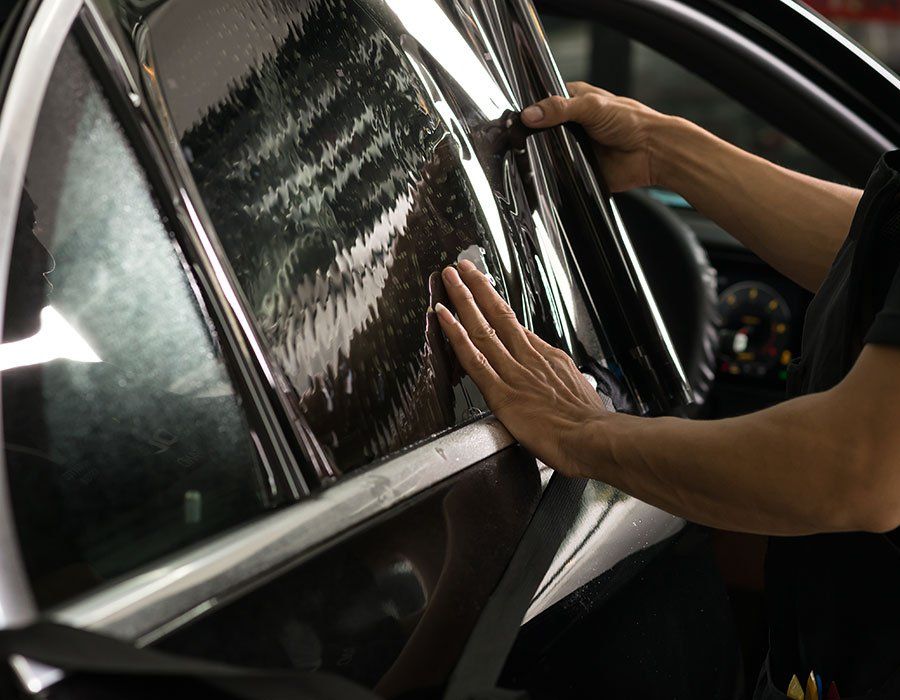 Person installing tinted film on a car window. Hands smoothing dark film onto glass inside vehicle.