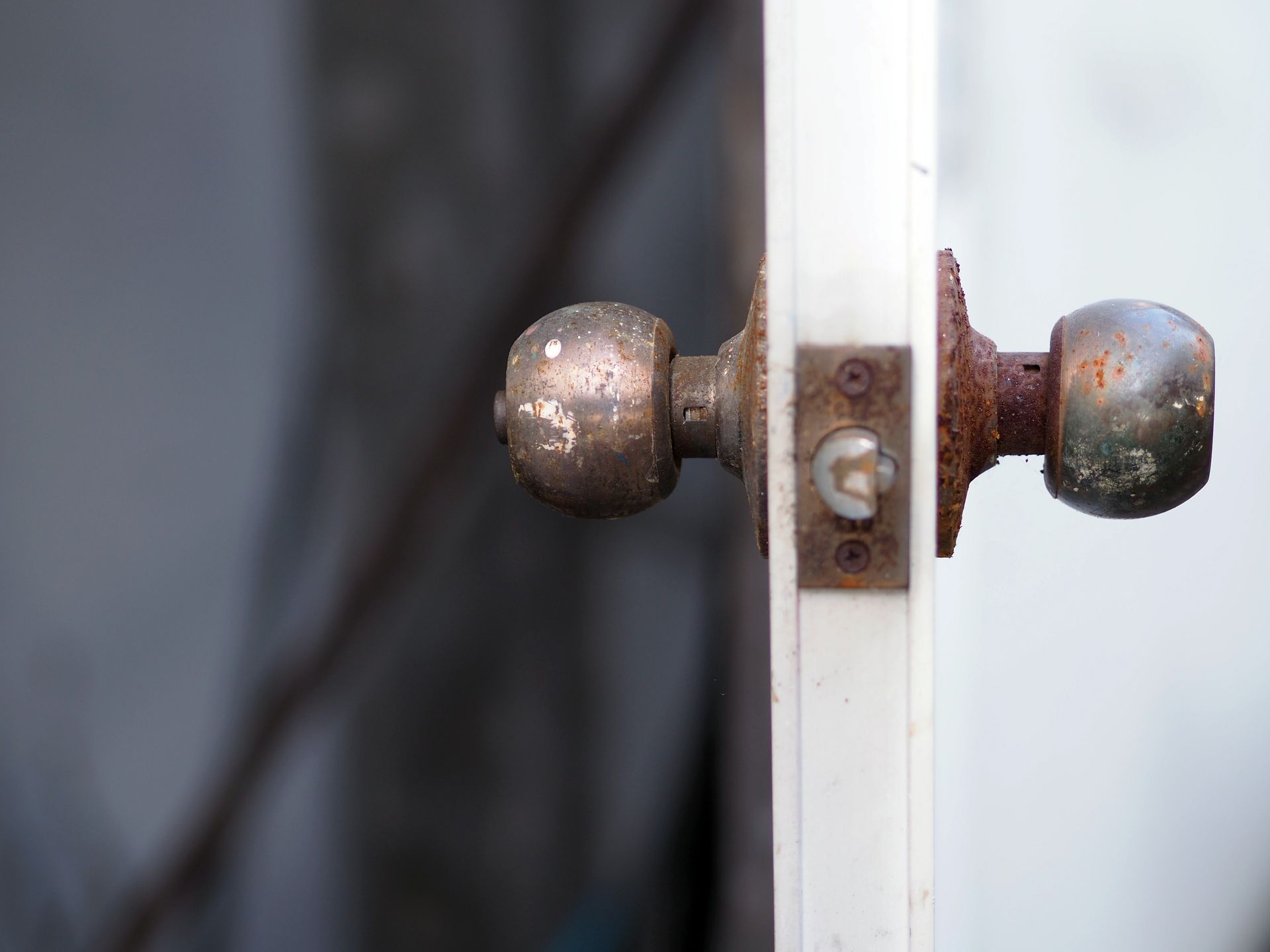 Rusty doorknob on a white door, slightly ajar, set against a blurred background.