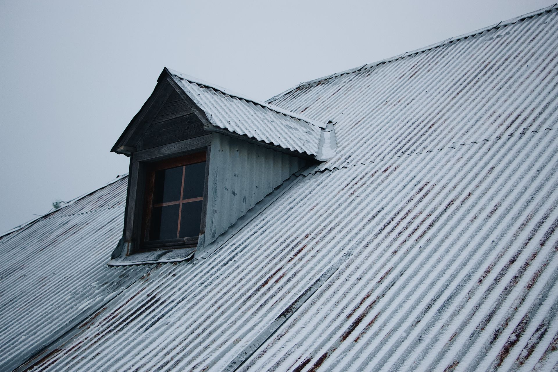 Snow-covered corrugated metal roof with a dormer window; overcast sky.