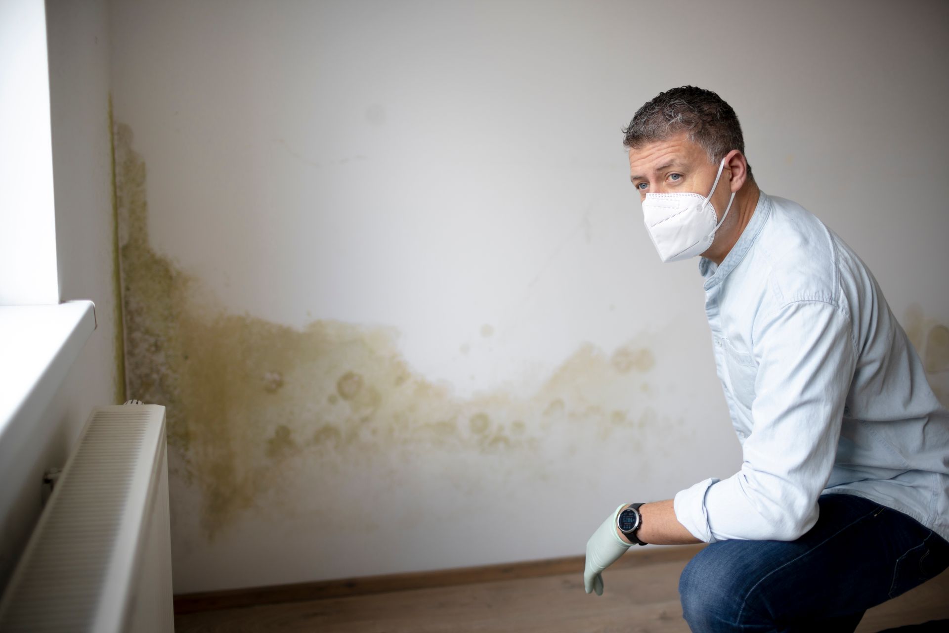 Man wearing mask examines wall with extensive mold.