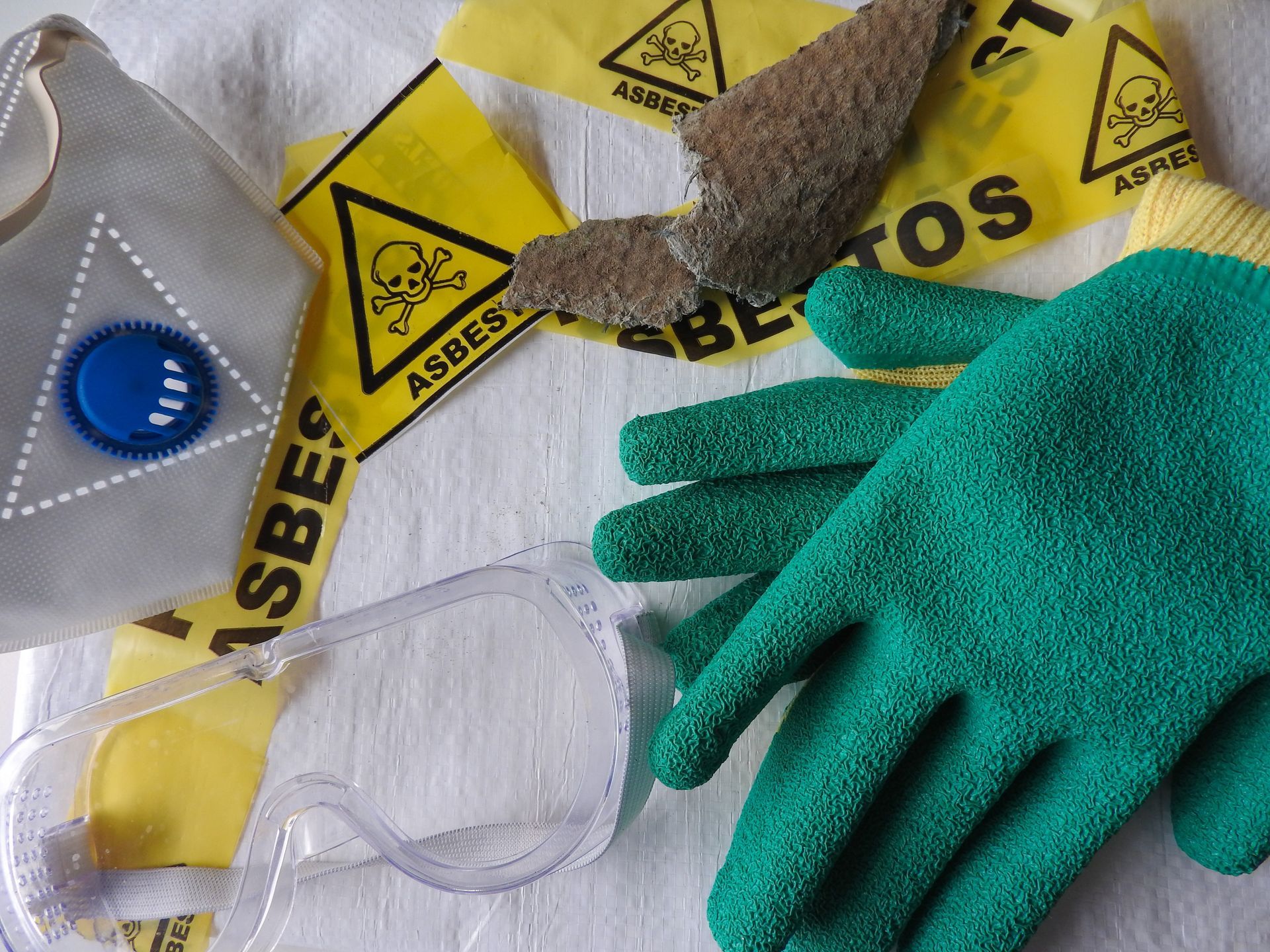 A pair of green gloves sitting on top of a yellow asbestos tape
