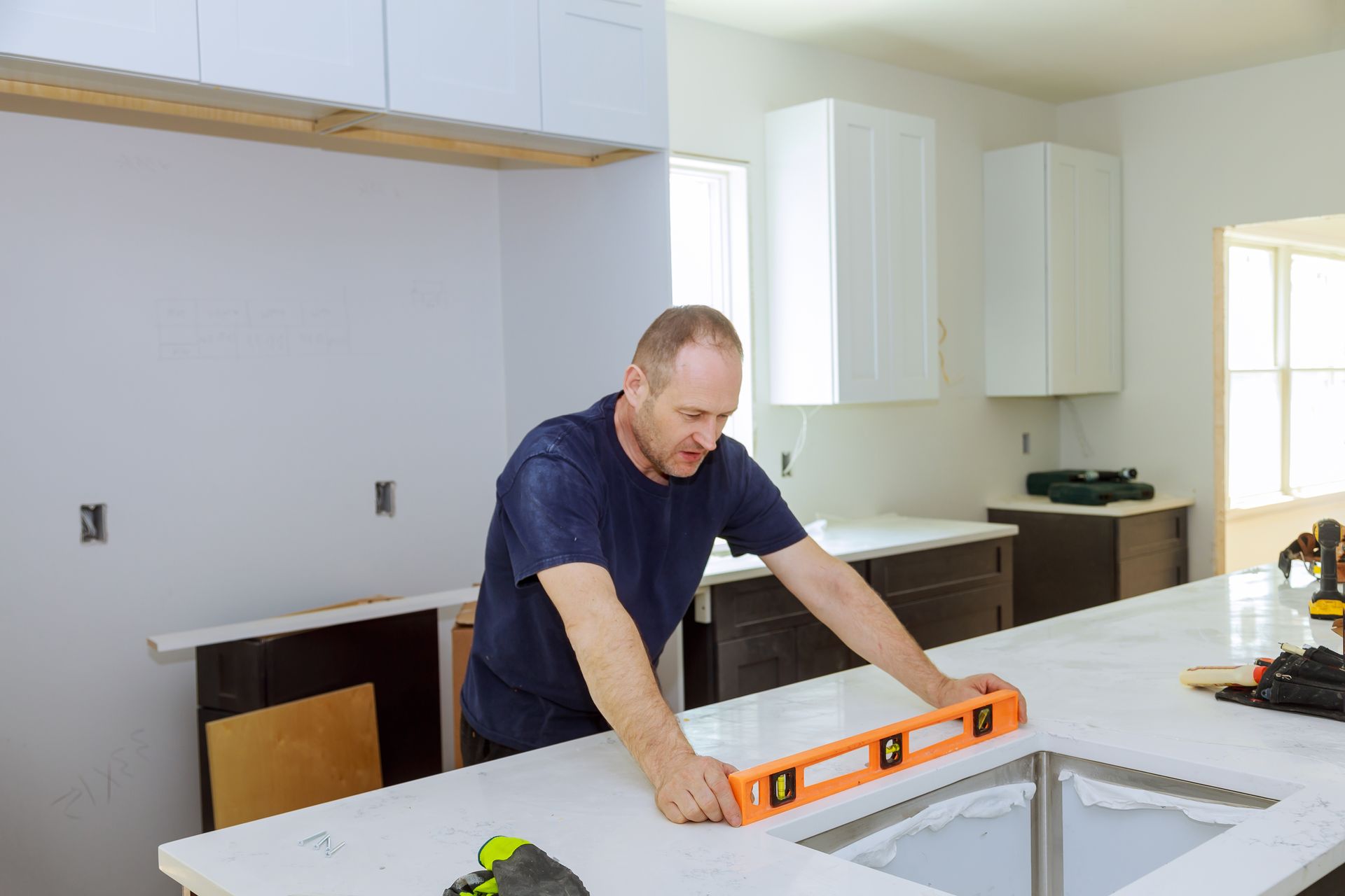 Man using a level on a kitchen countertop during cabinet installation.