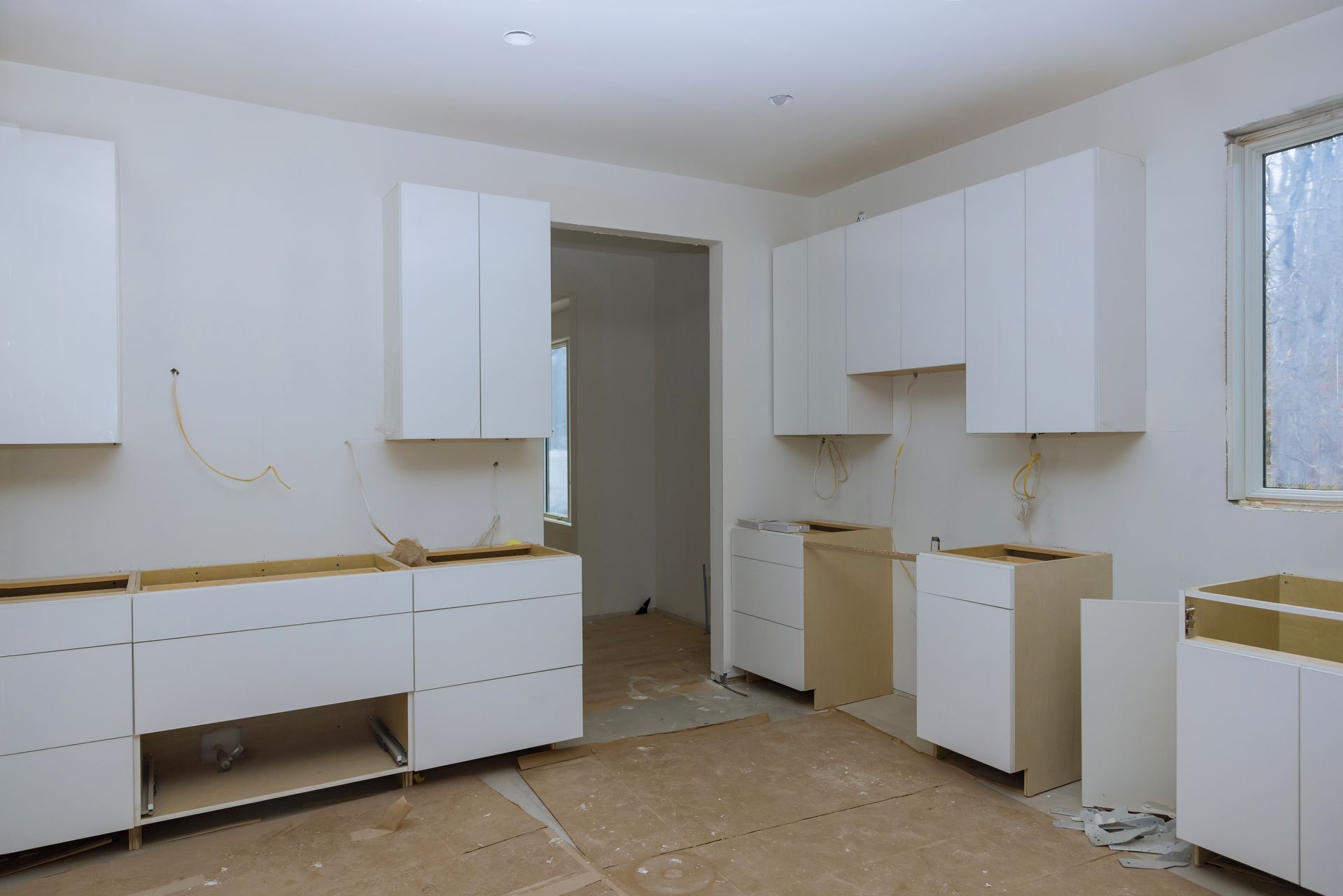 Kitchen under construction with white cabinets and unfinished base cabinets.