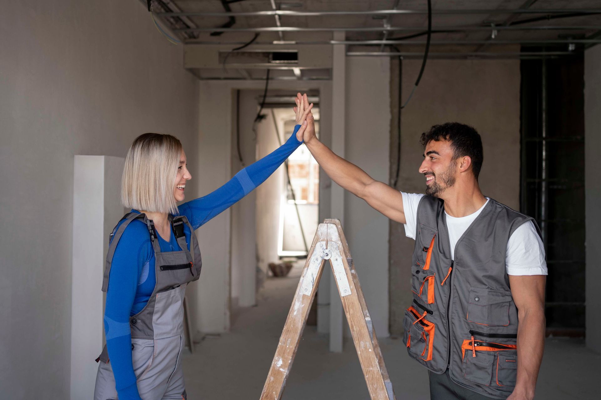 a man and a woman are giving each other a high five while standing next to a ladder .