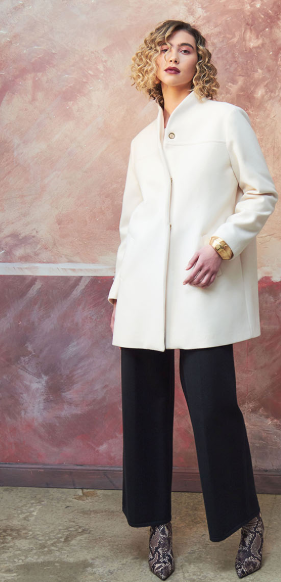 Donna in camice bianco e pantaloni neri, in piedi, sfondo rosa e marrone testurizzato.