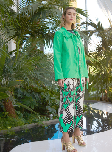 Donna che indossa una giacca verde e pantaloni a fantasia, in piedi all'aperto vicino alle piante.