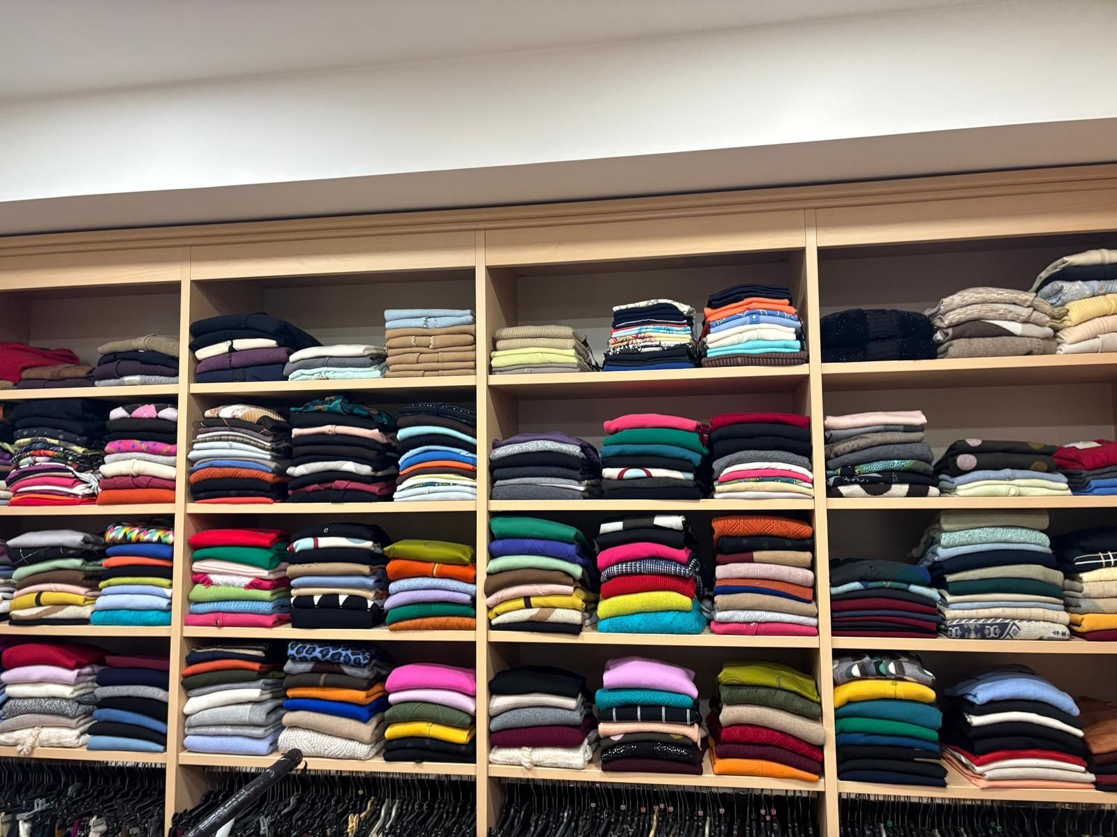 Scaffali pieni di maglioni ordinatamente piegati di vari colori in un negozio di abbigliamento.