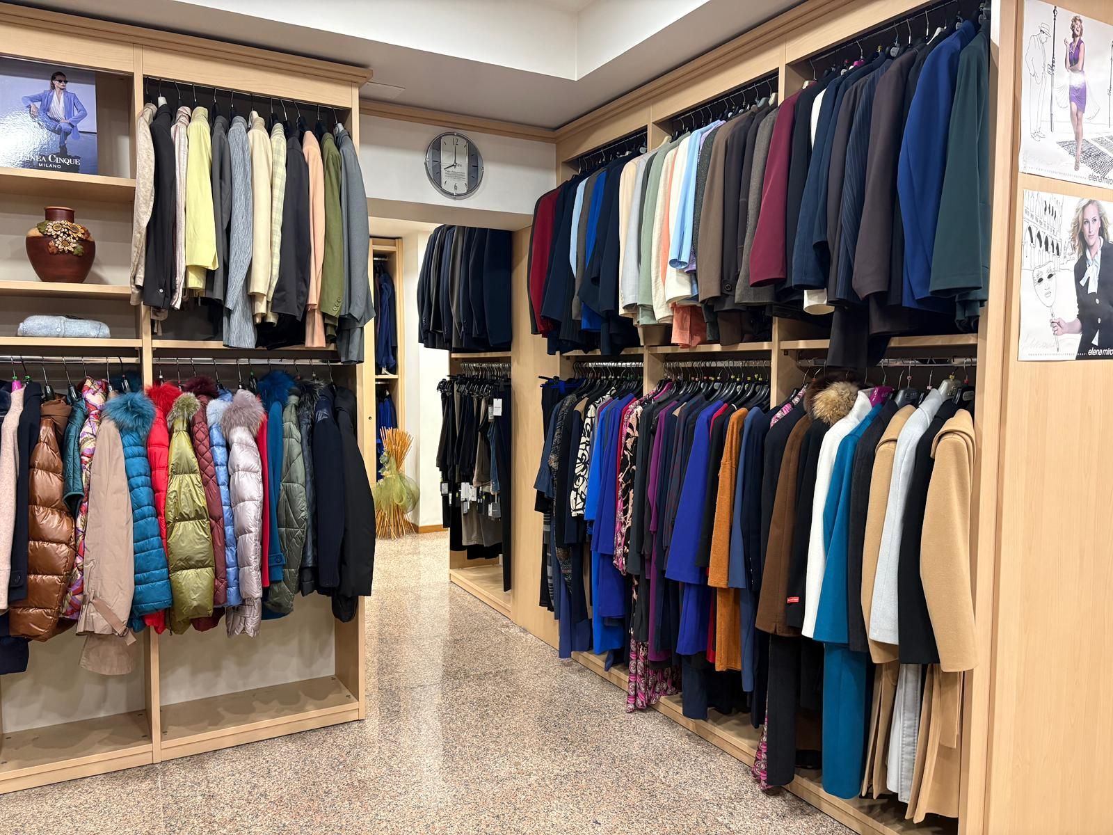 Interno di un negozio di abbigliamento con scaffali pieni di giacche, cappotti e abiti, e scaffali con gli articoli esposti.