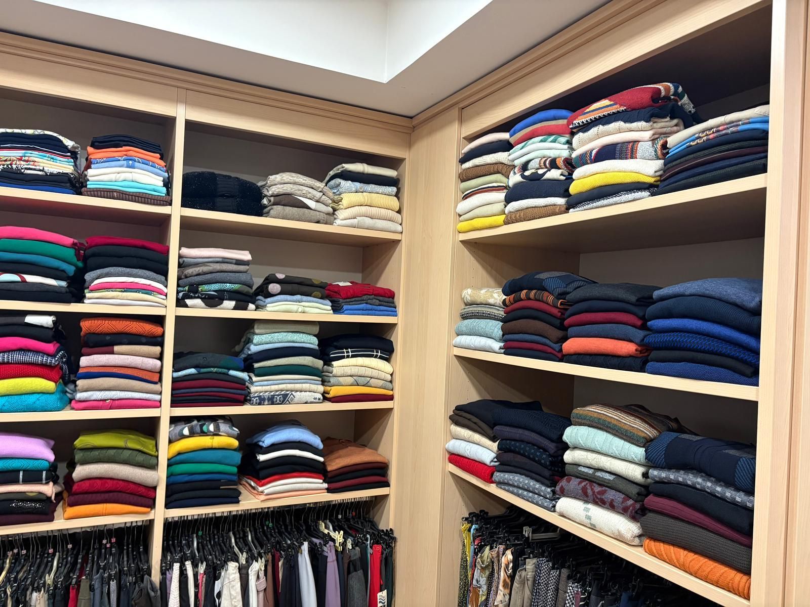 Ripiani di legno dell'armadio pieni di maglioni ordinatamente piegati in vari colori.