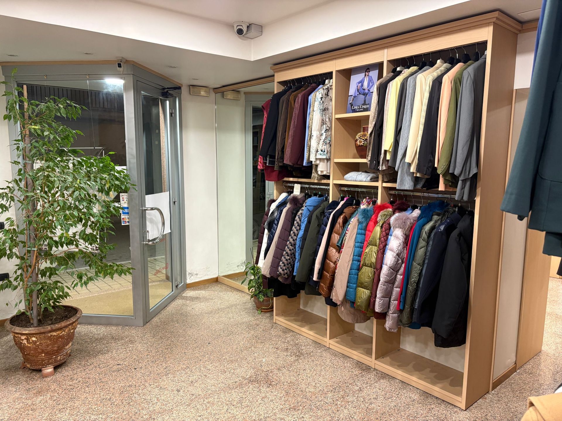 Interno di un negozio di abbigliamento con scaffali pieni di giacche e camicie.