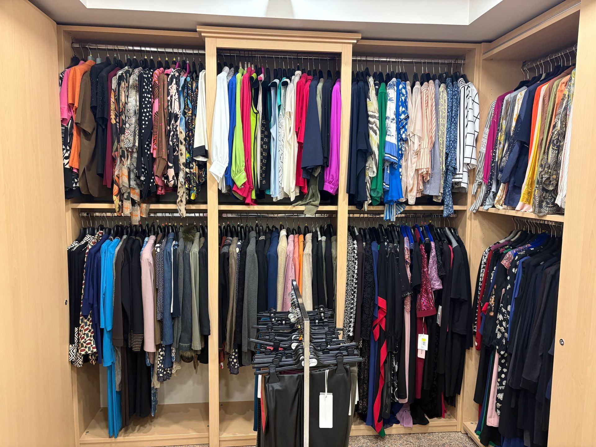 Armadio pieno di vestiti colorati appesi su grucce. Struttura in legno e pareti neutre.
