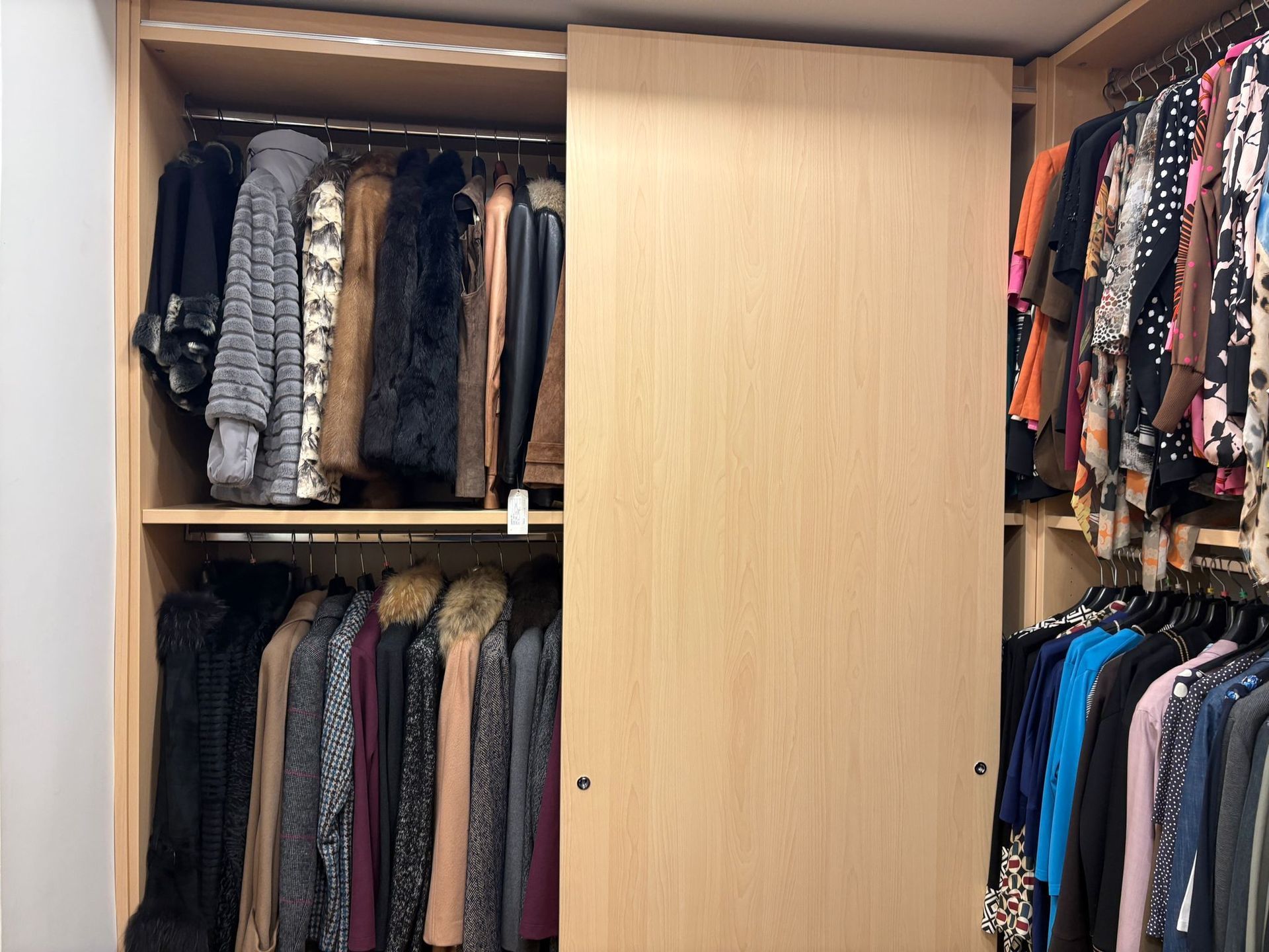 Armadio con ante scorrevoli in legno. I vestiti sono appesi alle aste: cappotti, vestiti e top.