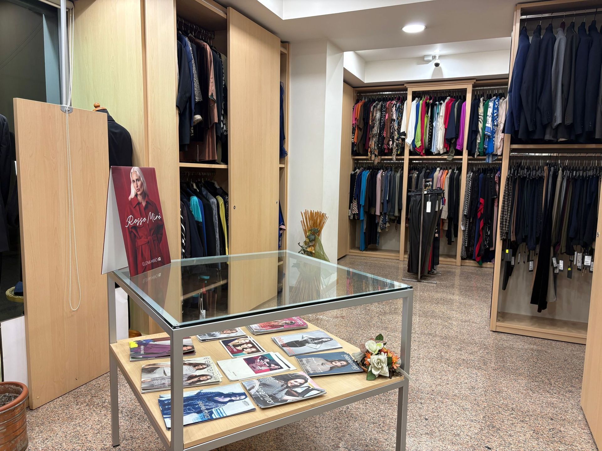 Interno di un negozio di abbigliamento con espositori per abiti e una vetrina con gli articoli.