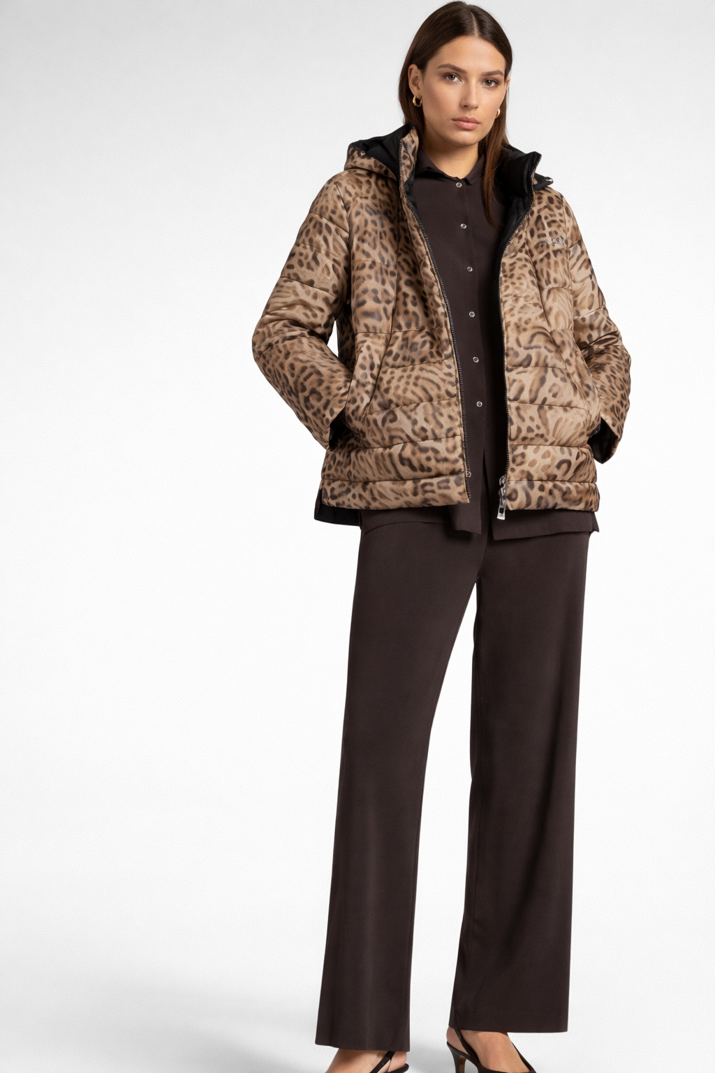 Donna in giacca leopardata e pantaloni scuri, in piedi in un ambiente interno.