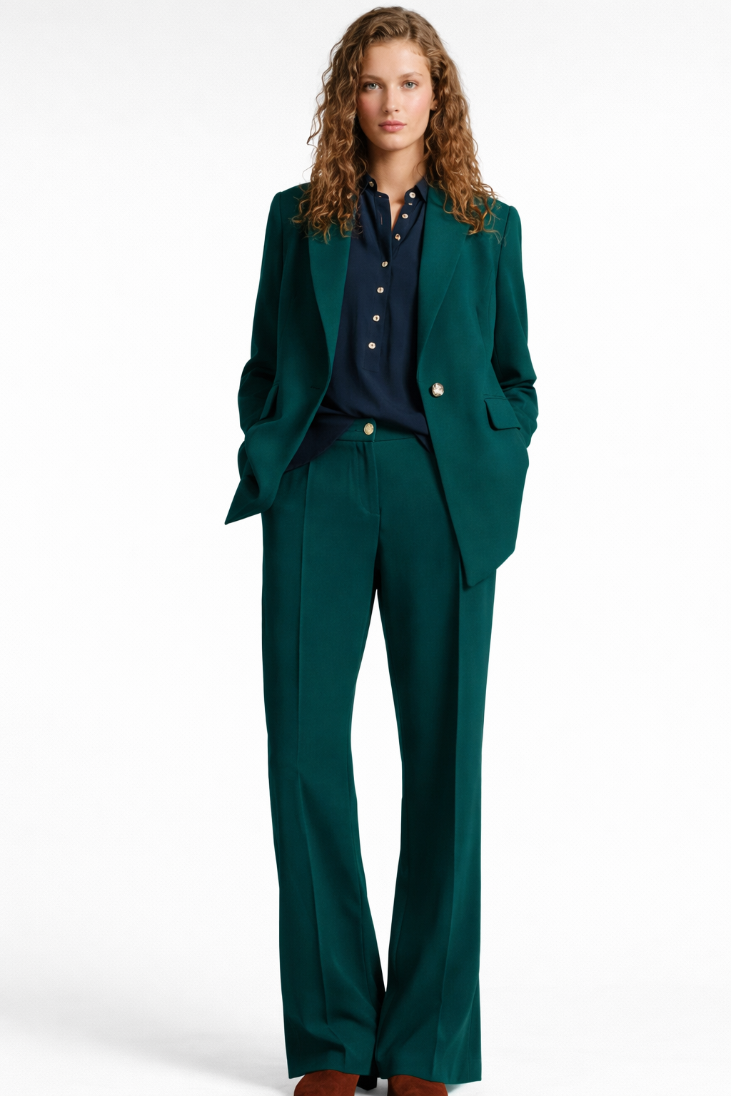 Donna che indossa un tailleur pantalone verde scuro e una camicia blu navy abbottonata; mani in tasca.