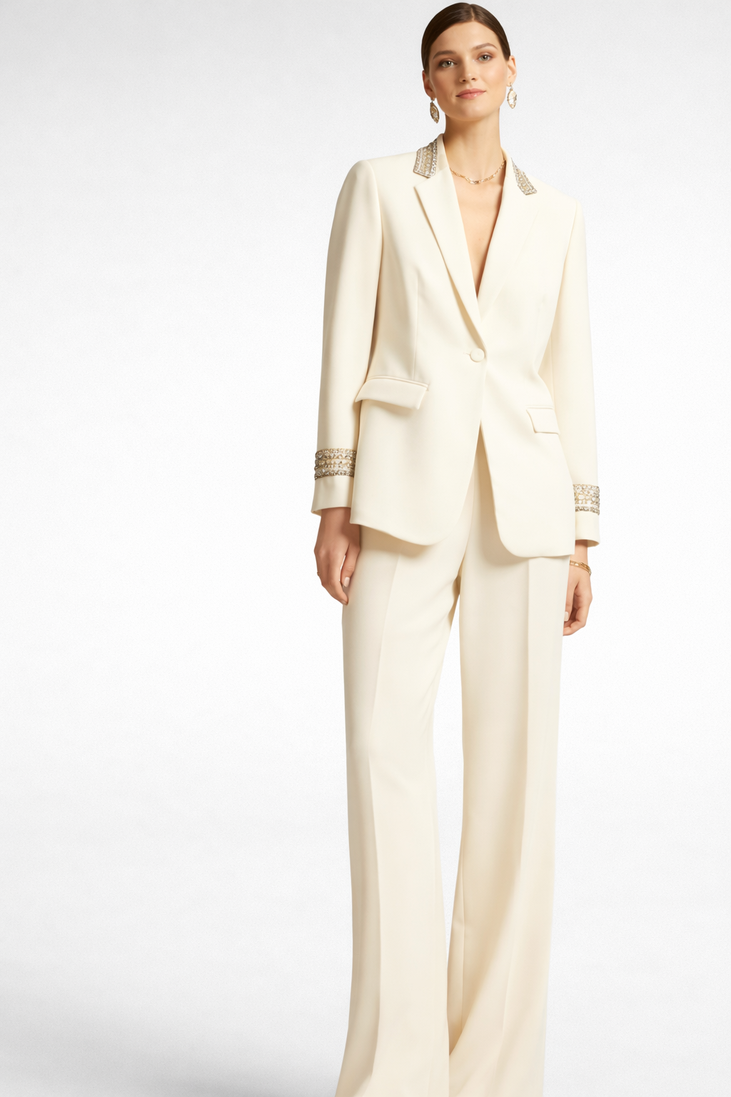 Donna in tailleur color crema, con revers e polsini decorati, in piedi su uno sfondo bianco.