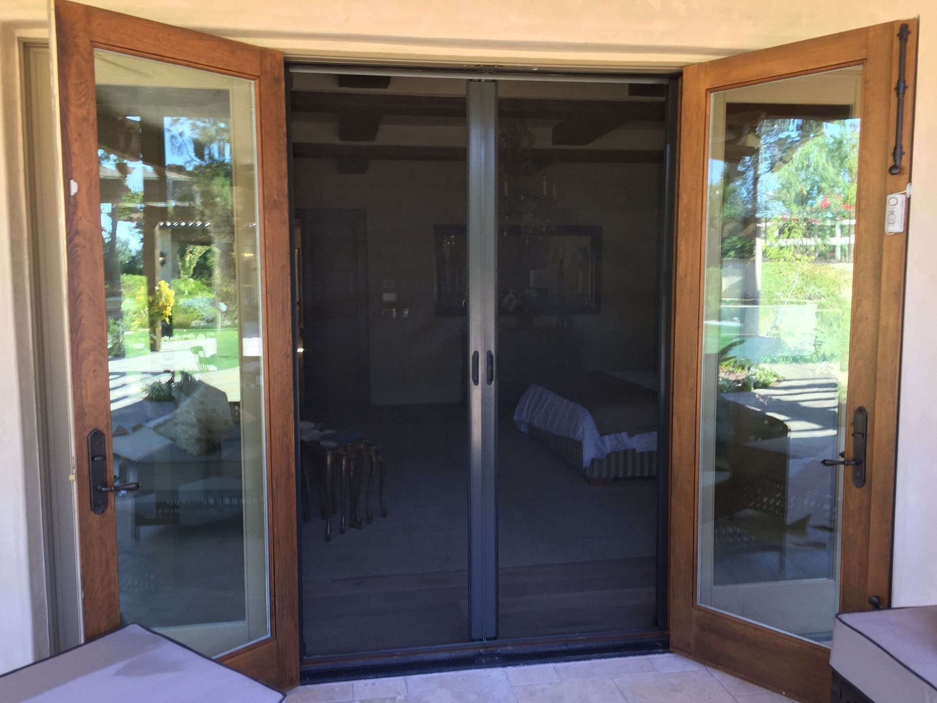 A screen door is open to a living room with a bed in the background.