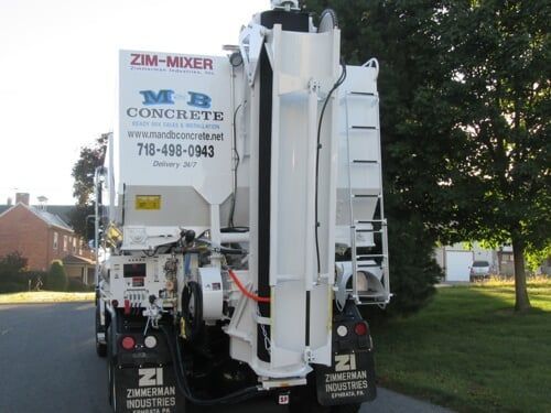 Concrete mixer truck parked on a street beside trees and houses