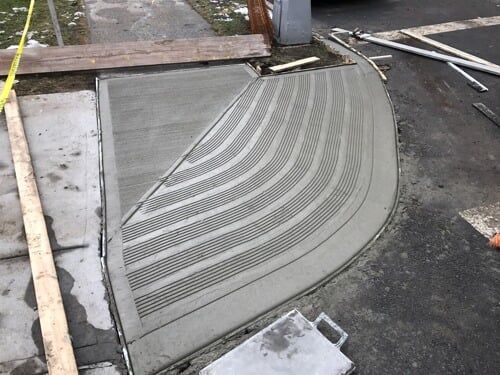 Curved tactile concrete ramp with raised grooves at a curb cut on a sidewalk/road edge