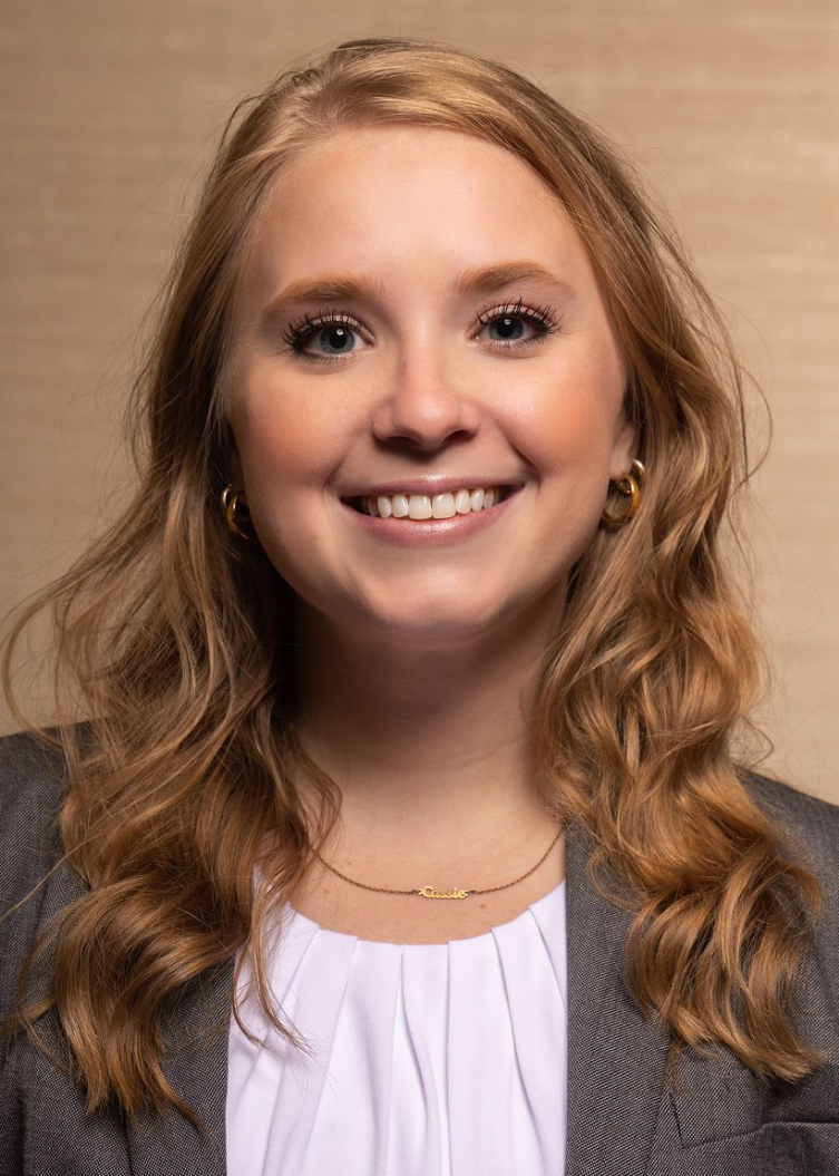 Shelby N. Clinging in a suit and white shirt is smiling for the camera .