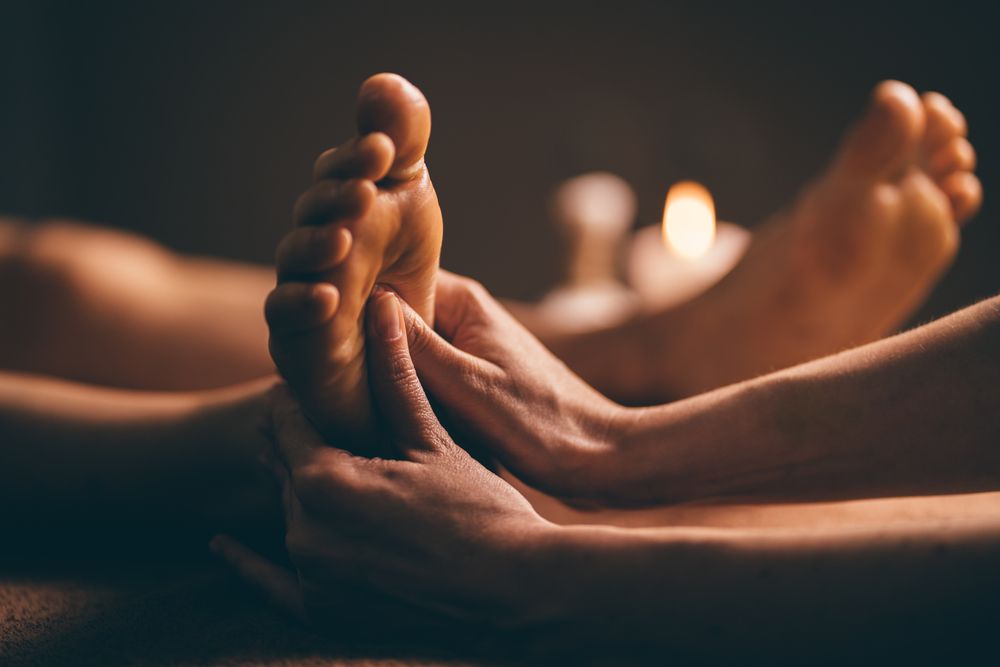 Hands Massaging a Foot; Candles in Background — Leela Thai Massage & Spa in Newtown, QLD