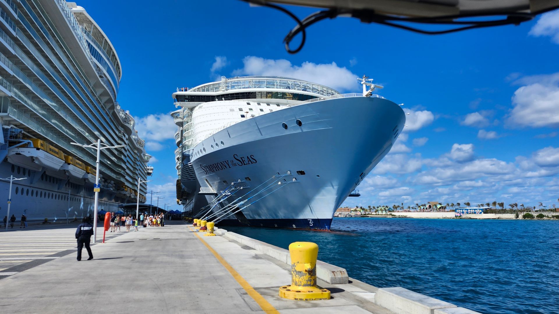 Cruise ship docked at a sunny harbor beside a waterfront promenade and blue water