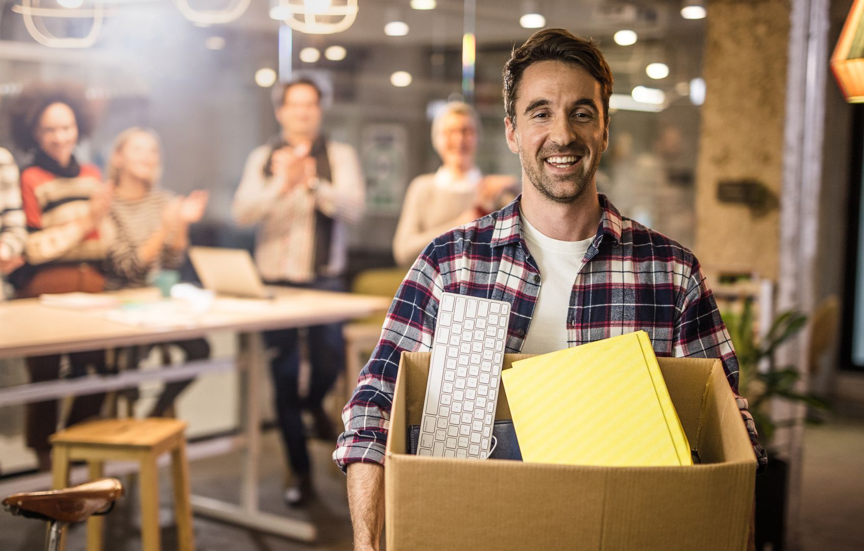 Man carrying a box of personal effects after leaving a job. He is smiling and surrounded by smiling