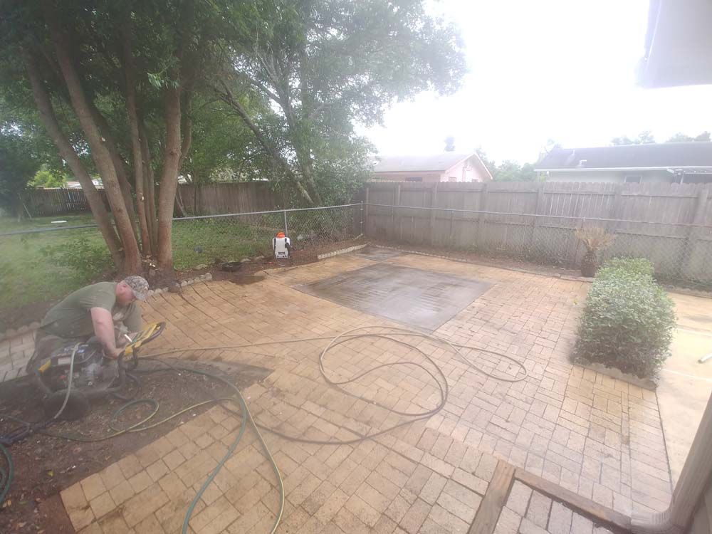 A man is cleaning a brick patio with a hose.