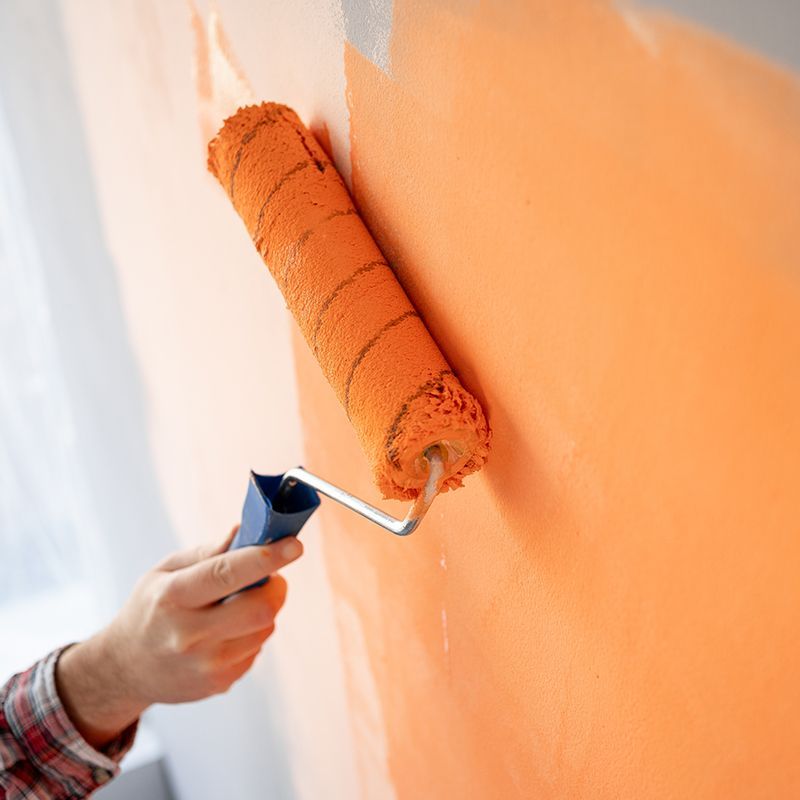 A person is painting a wall with an orange paint roller