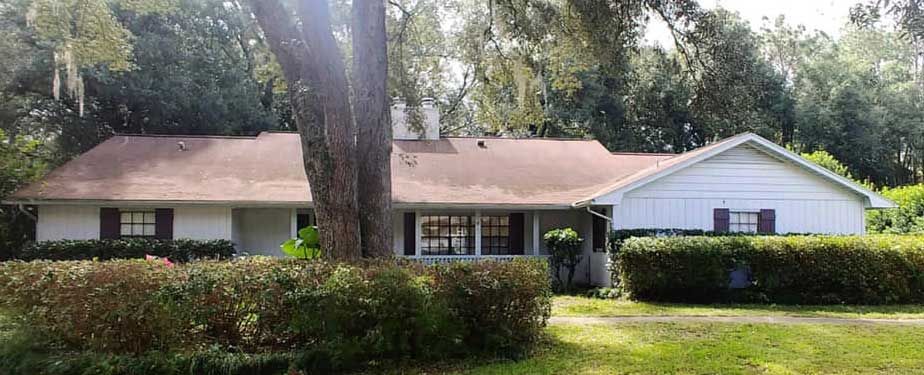 A white house with a red roof is surrounded by trees and bushes.