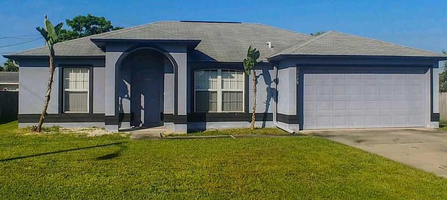 A gray house with a gray roof and a lush green lawn in front of it.