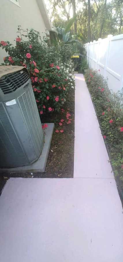 A walkway leading to a house with a fence and flowers.