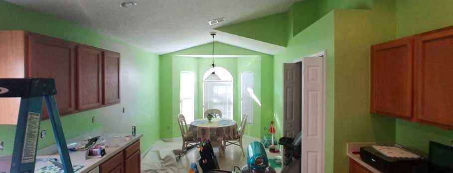 A kitchen with green walls and wooden cabinets is being painted.