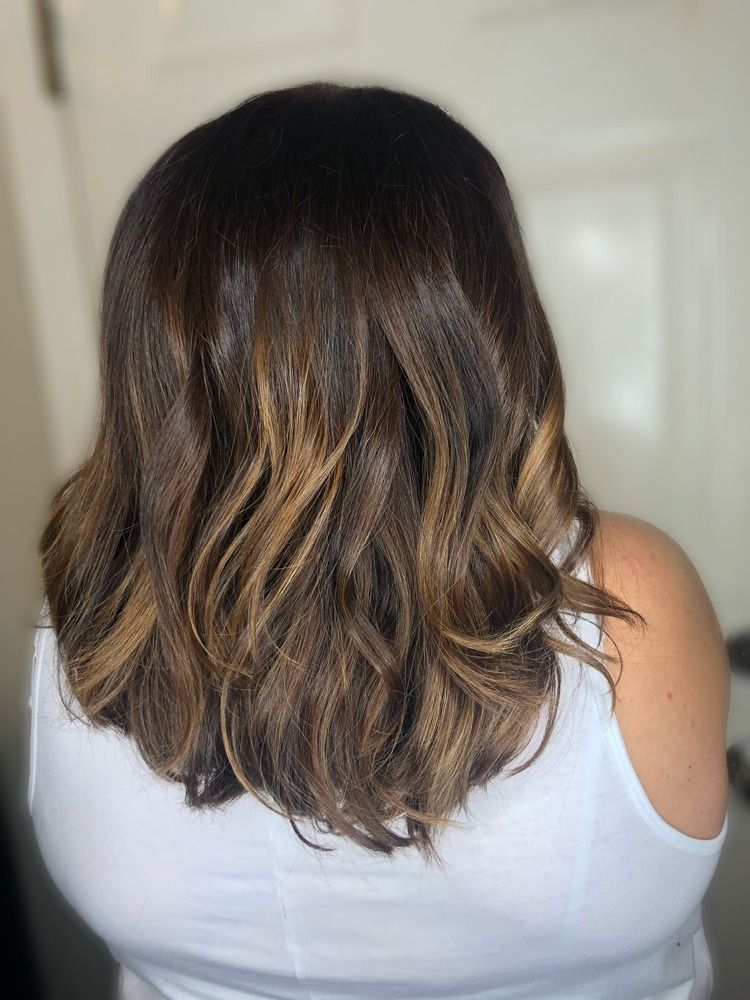 A woman with long brown hair is wearing a white tank top.