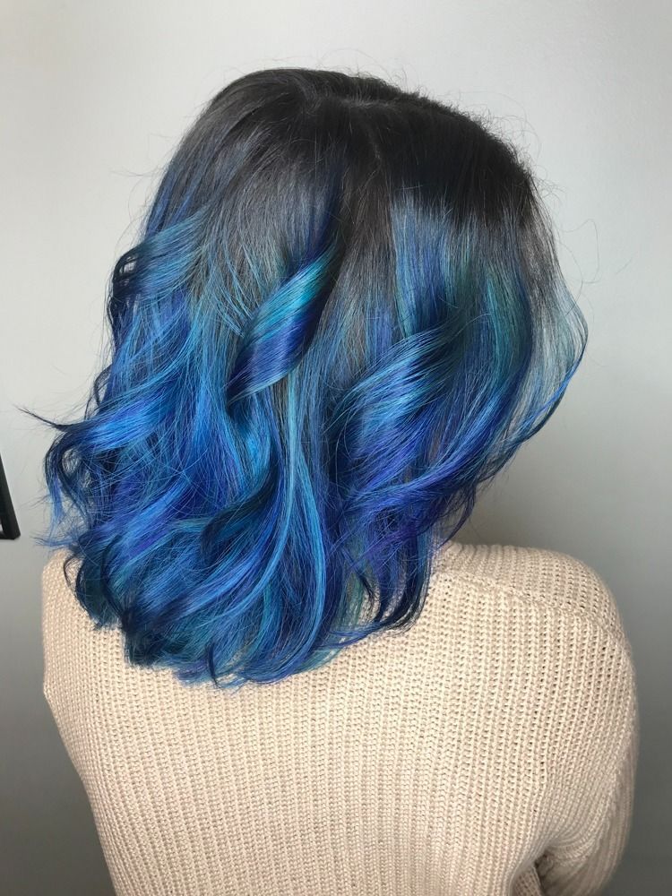 A woman with blue hair is wearing a white sweater.