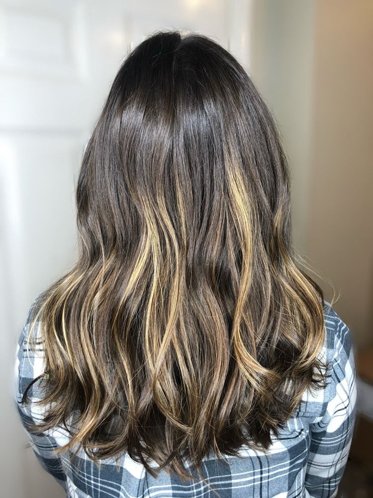 A woman with long brown hair and blonde highlights is wearing a plaid shirt.