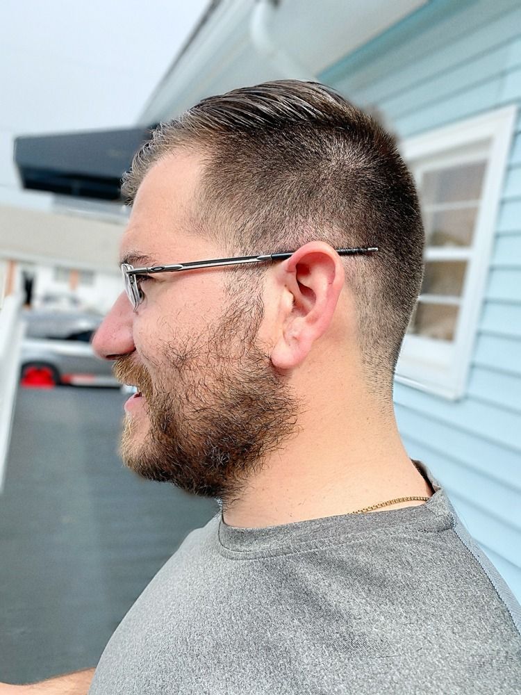 A man with glasses and a beard is standing in front of a blue house.