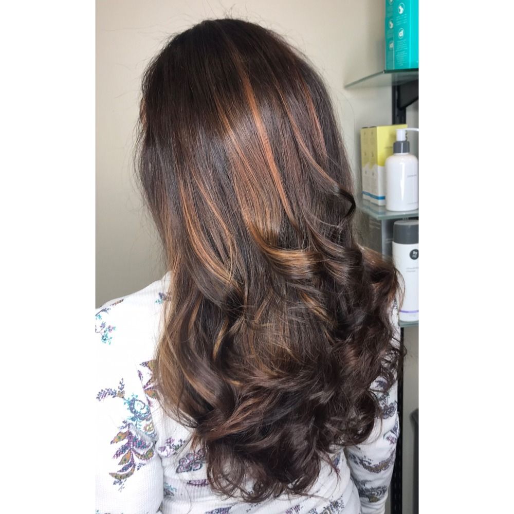 A woman with long brown hair is standing in front of a shelf with bottles of hair products.