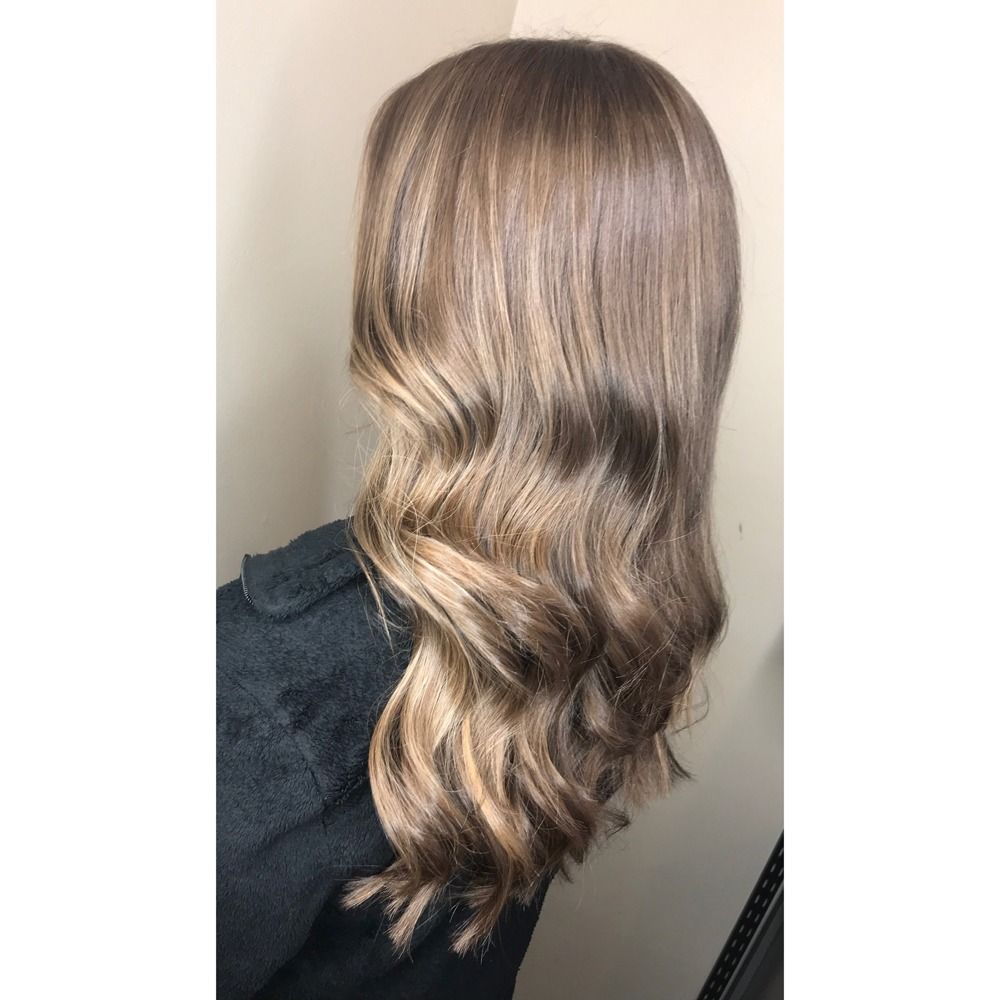 A woman with long brown hair is standing in front of a wall.