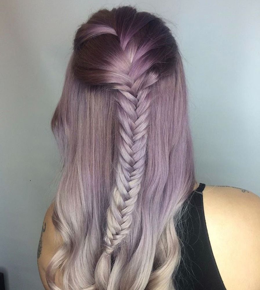 A woman with purple hair is wearing a braided half up half down hairstyle.