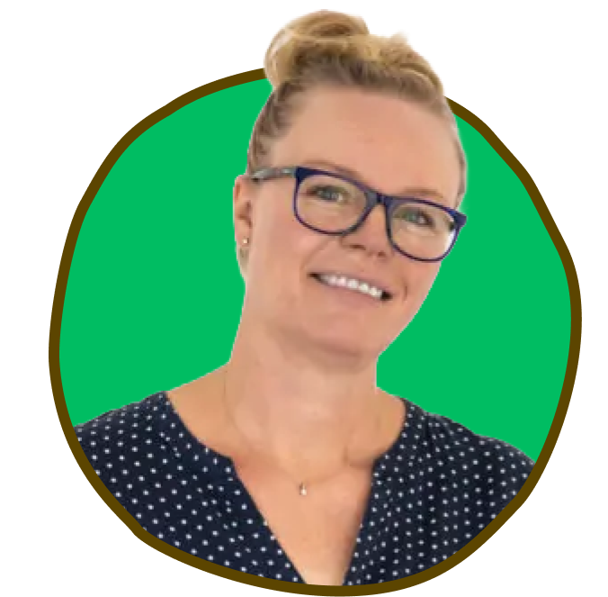 Kvinde med briller, smilende, hår i en knold, iført en prikket skjorte, grøn baggrund.