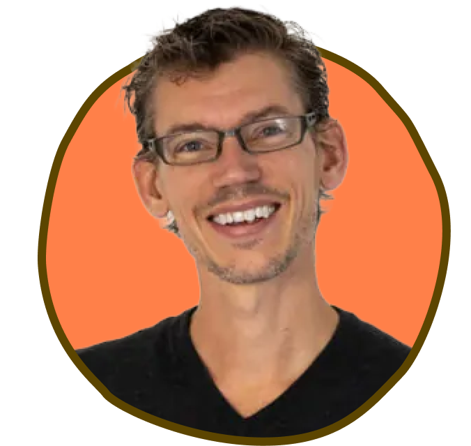 Smilende mand med briller og skægstubbe i en brunkantet orange cirkel, iført en sort skjorte.