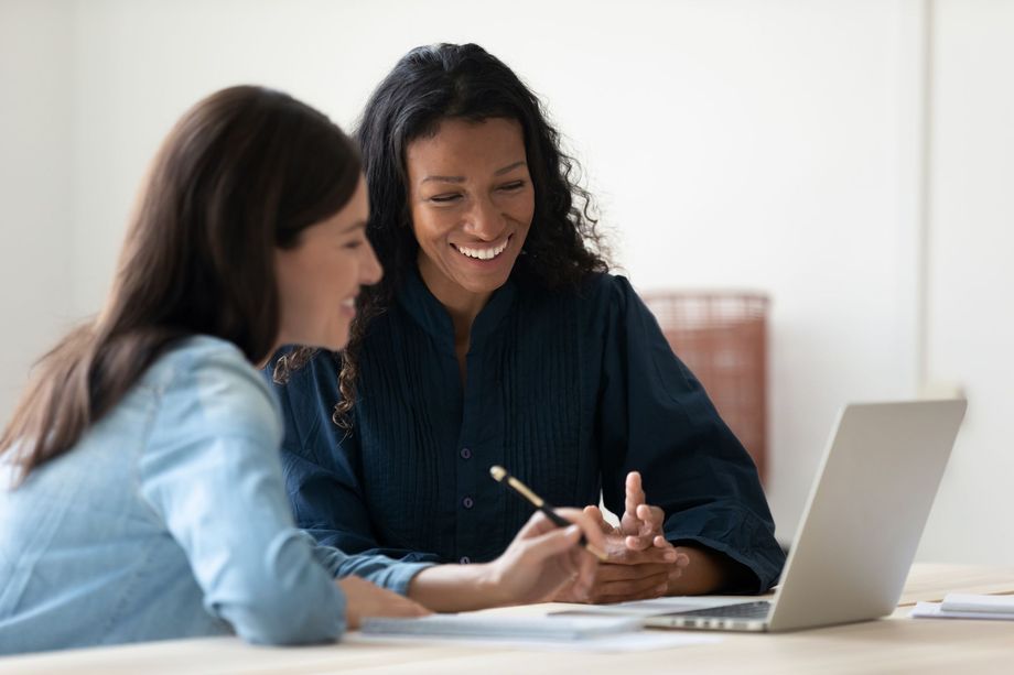 two women are sitting at a table looking at a laptop computer