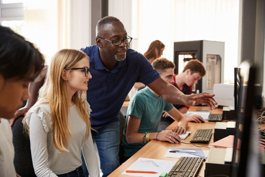 a man is teaching a girl how to use a computer in a classroom