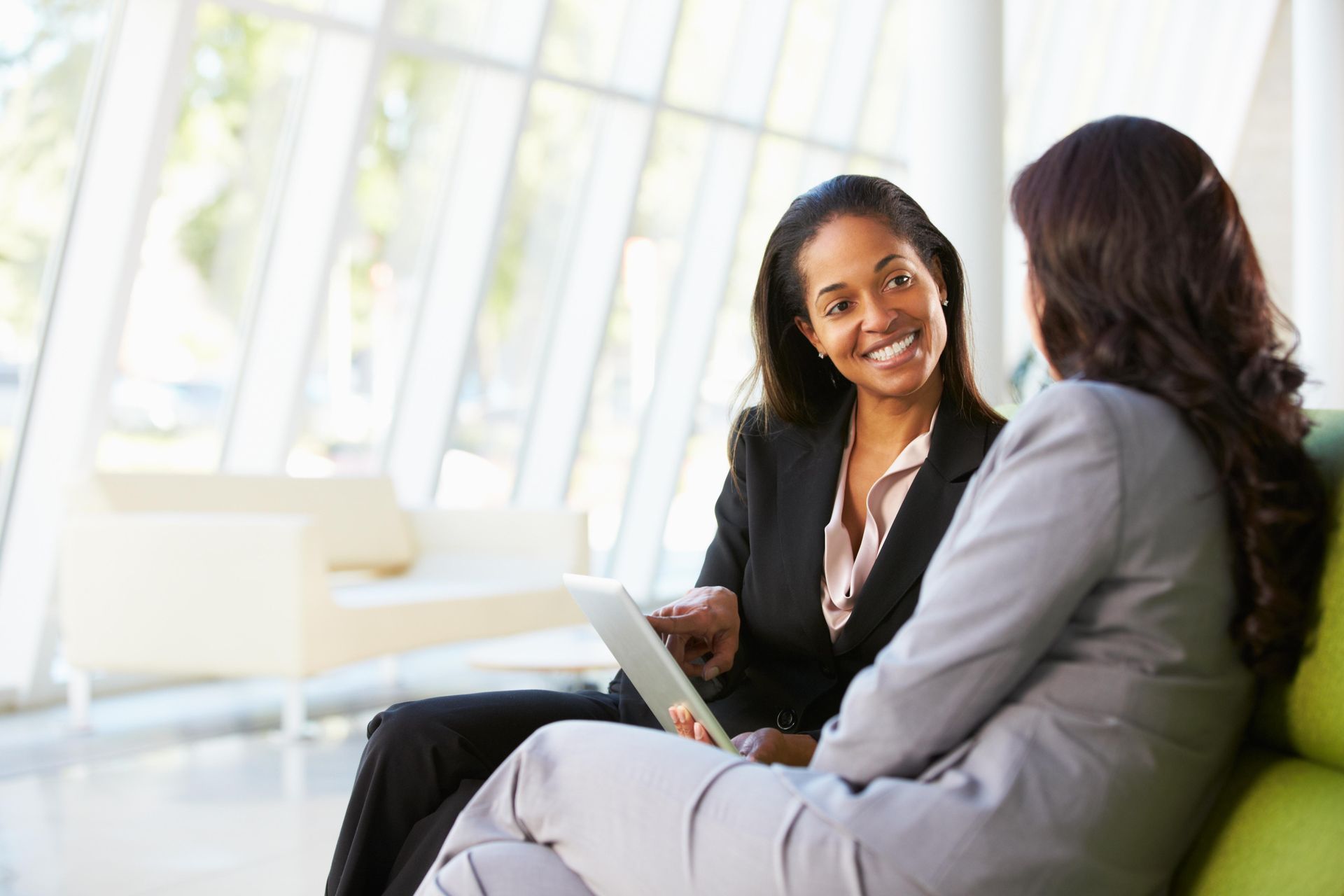 two women are sitting on a couch looking at a tablet