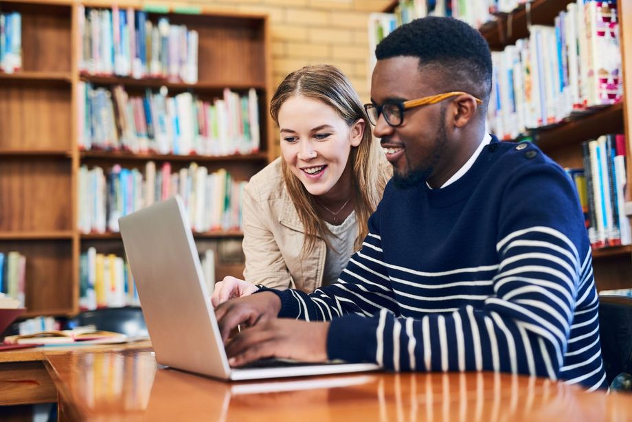 a man and a woman are looking at a laptop in a library