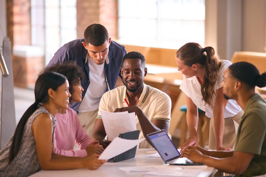 a group of people are sitting around a table looking at papers and a laptop