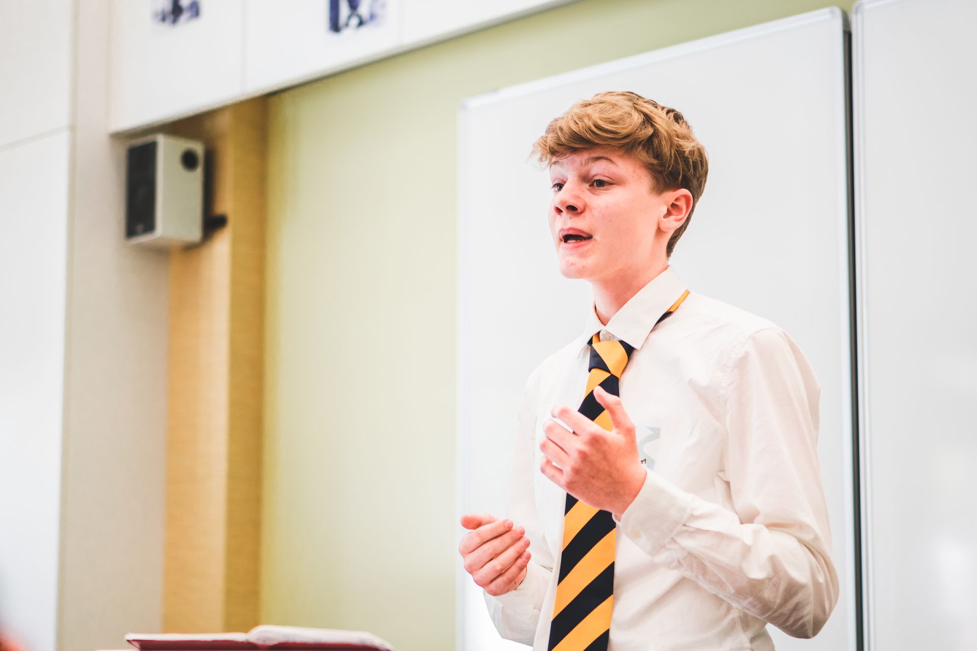 A young boy is giving a speech in front of a whiteboard in a classroom.