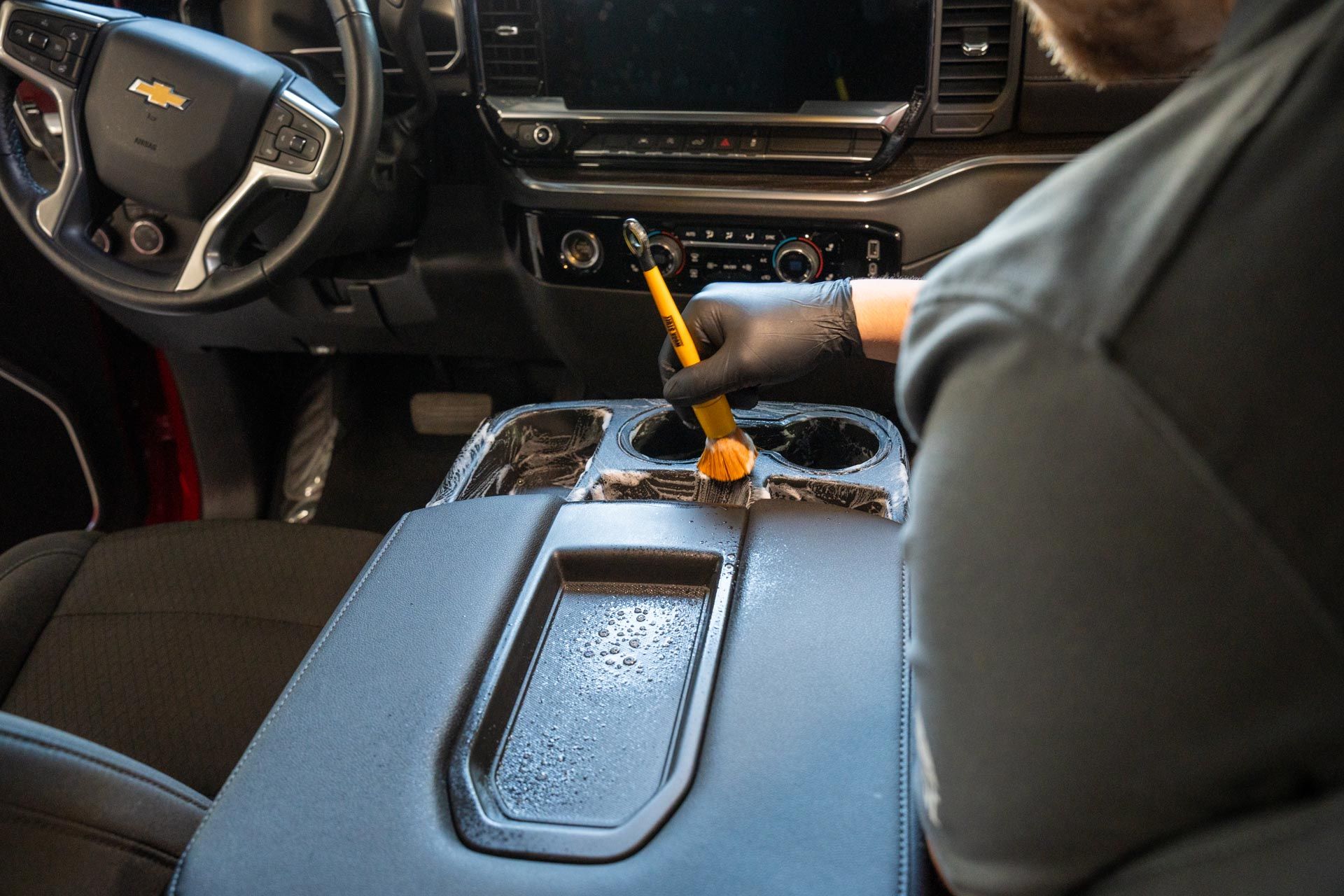 A man is cleaning the dashboard of a car with a brush.