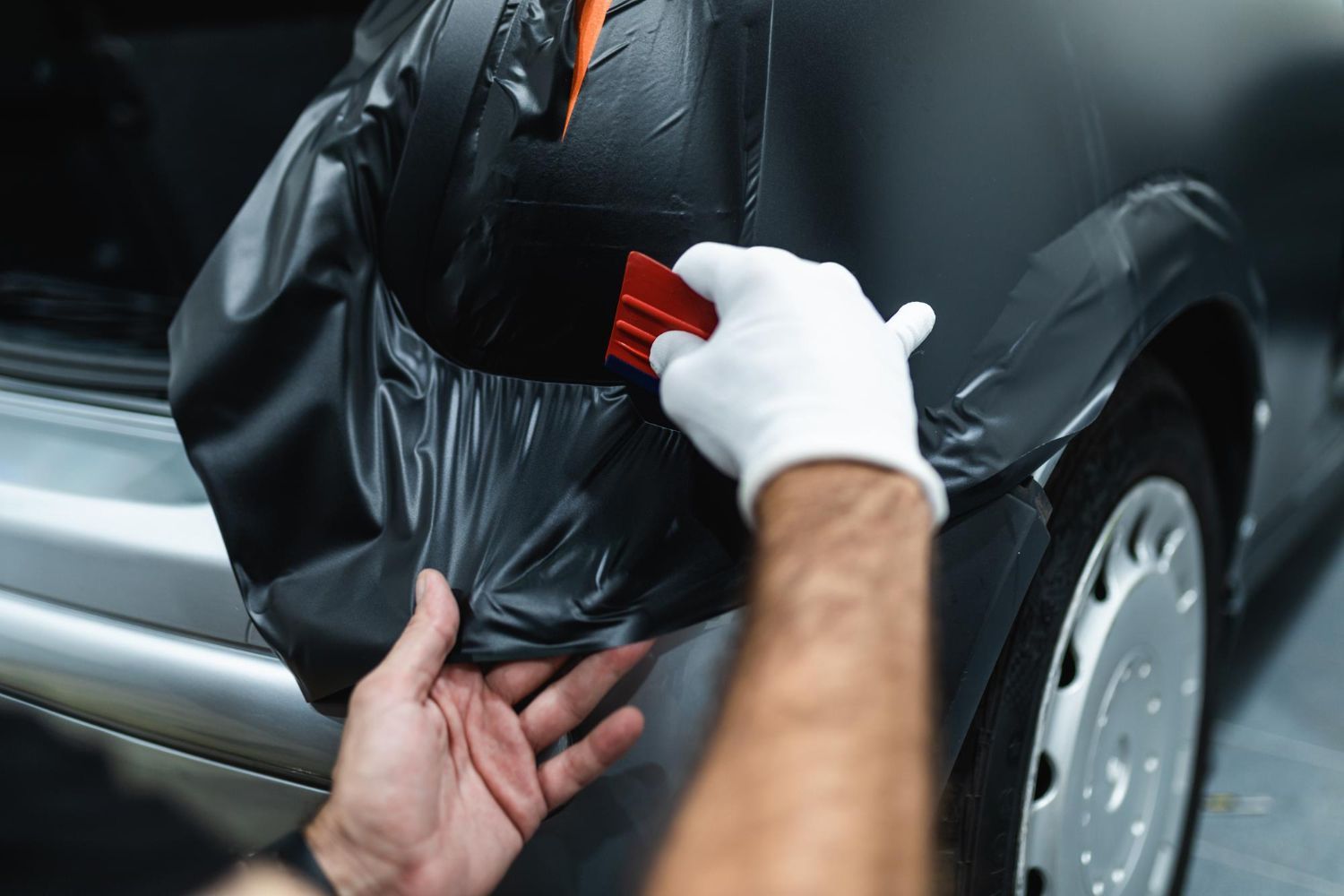 A man is wrapping a car in black vinyl wrap.